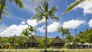 A tropical resort with two bungalow-style buildings, surrounded by palm trees and lush greenery, under a clear blue sky. - Pure Magnetic Villa 1 (Nelly Bay)
