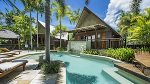 Un resort con piscina, sillas de descanso y exuberante jardinería tropical.