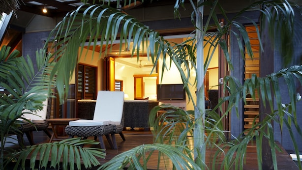 A cozy outdoor seating area with a cushioned chair and a small table, surrounded by lush tropical plants.