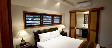 A bedroom with a bed, two bedside lamps, a ceiling fan, and a window with a view of a wooden deck.