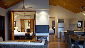 A modern hotel room with a sofa, a TV, a bed, a desk, and a kitchen area.