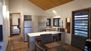 A modern kitchen with a central island, wooden flooring, and a dining area with two chairs. - Pure Magnetic Villa 8 (Nelly Bay)