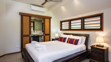 A neatly made bed with white linens and colorful pillows, a bedside table with a lamp, and a ceiling fan.