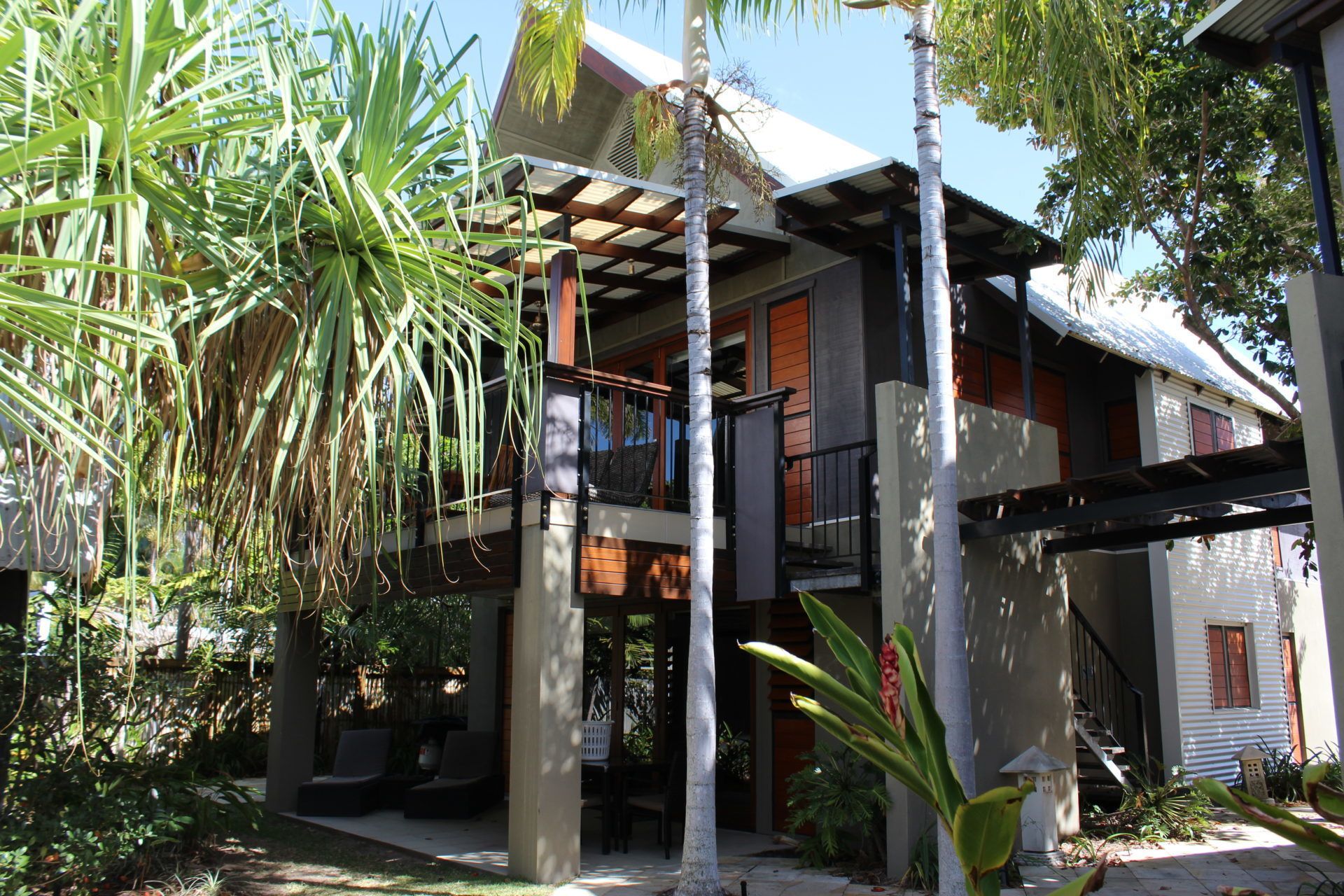 A two-story house with a balcony, surrounded by tropical plants.