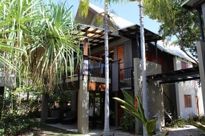 A two-story house with a balcony, surrounded by tropical plants.