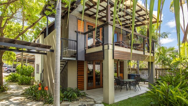 Une maison à deux étages dotée d’un patio couvert, d’un espace salon extérieur et d’un escalier menant à l’étage supérieur.