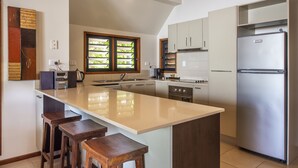 Une cuisine moderne dotée d’un grand îlot central, de tabourets de bar, d’appareils électroménagers en acier inoxydable et offrant une vue sur la verdure par la fenêtre.