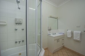 A modern bathroom with a glass-enclosed shower, a white sink with a mirror above, and a beige-tiled floor.