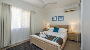 Une chambre d’hôtel comprenant un lit, deux tables de chevet, un ventilateur de plafond et un appareil de climatisation.