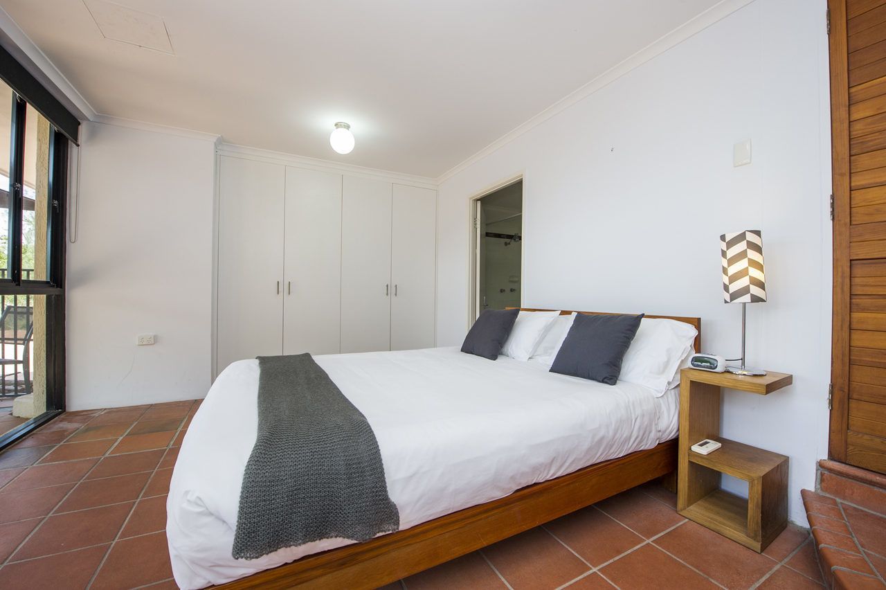 Een slaapkamer met een bed, nachtkastje, spiegel en garderobe.