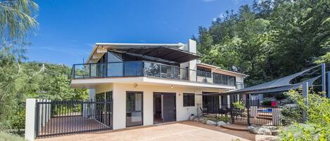 A modern two-story house with a balcony, a paved driveway, and a fenced yard.
