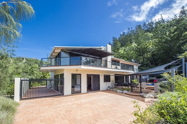 A modern two-story house with a balcony, a paved driveway, and a fenced yard. - The Beach House at Arthur Bay (Florence Bay)