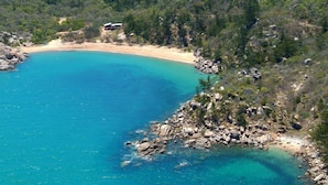 Une zone côtière caractérisée par une plage de sable, des eaux turquoise et limpides, et un terrain rocheux.