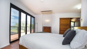 Une chambre dotée d’un grand lit, d’une tête de lit en bois, d’une porte-fenêtre coulissante donnant sur un balcon et d’une petite fenêtre avec vue.