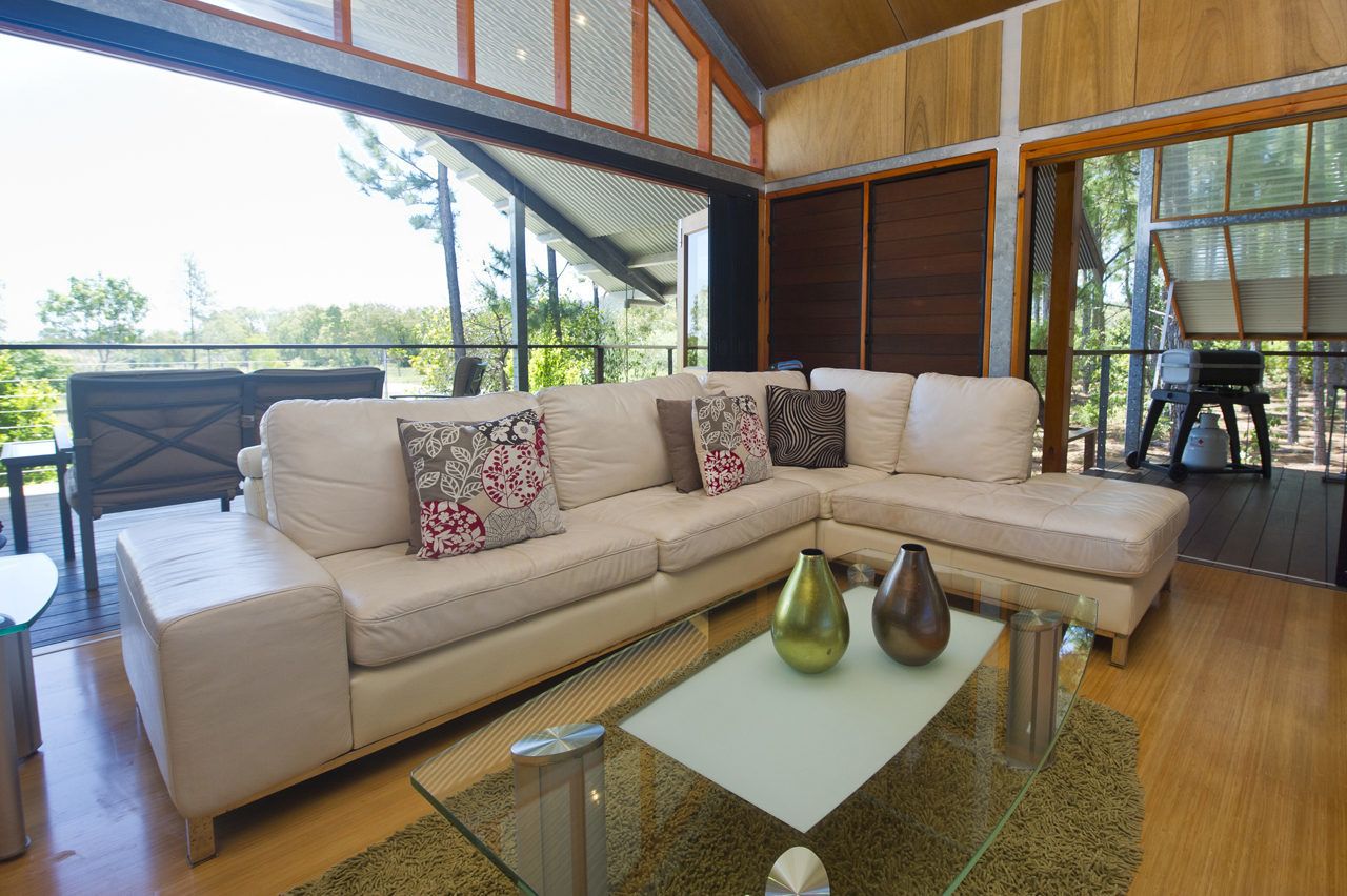 A modern living room with a beige sectional sofa, glass coffee table, and large windows offering a view of the outdoors.