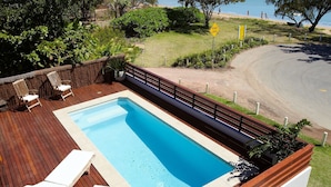 A swimming pool with lounge chairs and a view of the beach and mountains. - Villa Kembali (Horseshoe Bay)
