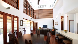 A spacious living area with a large dining table, multiple seating options, a television, and a kitchen area. - Villa Kembali (Horseshoe Bay)
