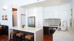 A modern kitchen with white cabinetry, a stainless steel refrigerator, a built-in oven, and a large island with bar stools. - Villa Kembali (Horseshoe Bay)