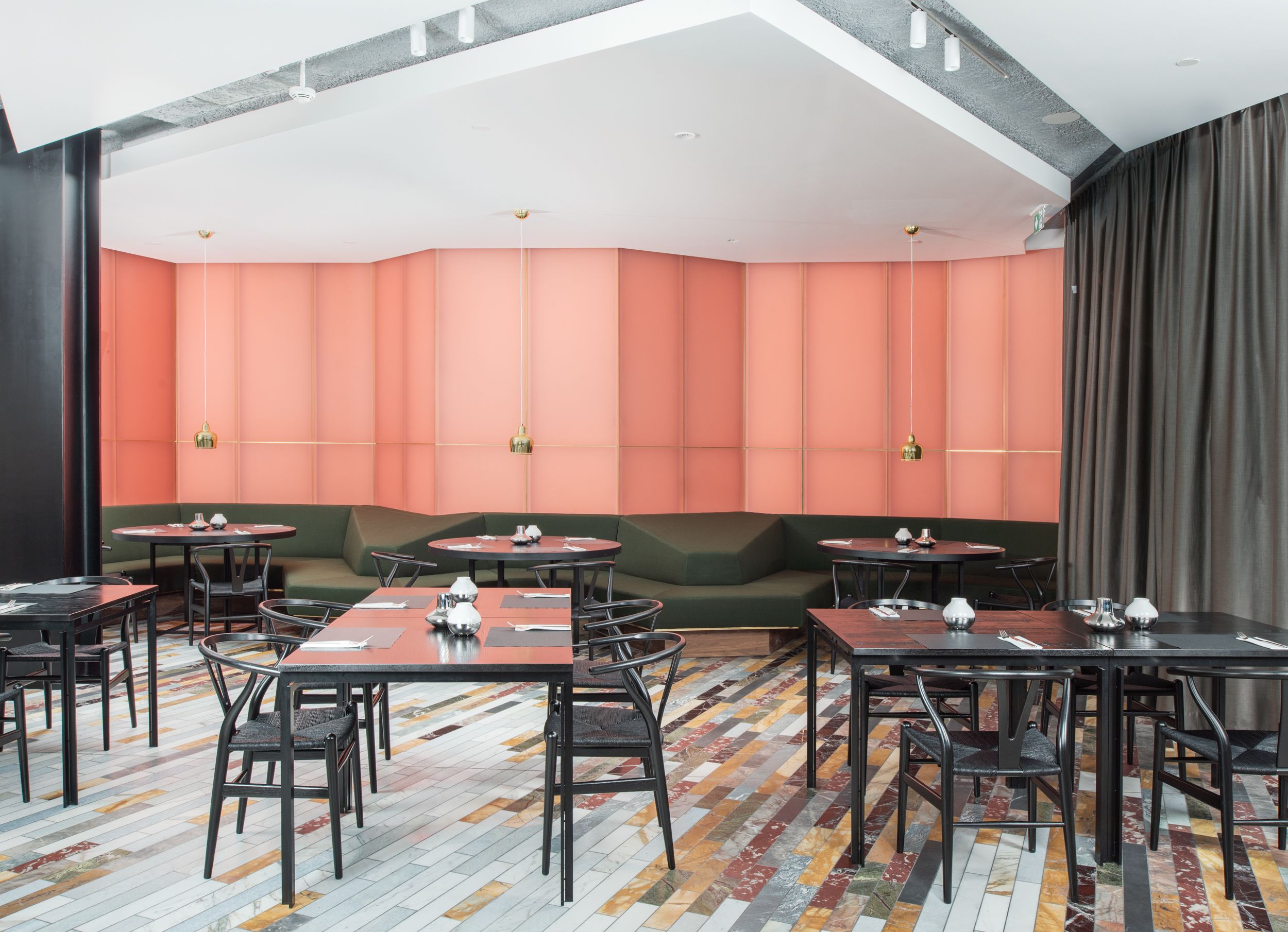 Un espace de restauration moderne avec des tables rondes et des banquettes, un sol à motifs et un plafond haut doté d’un éclairage encastré.