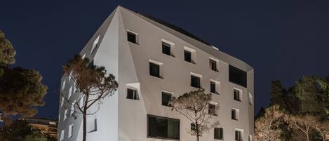 A modern building with a geometric facade, multiple windows, and a tree in front.