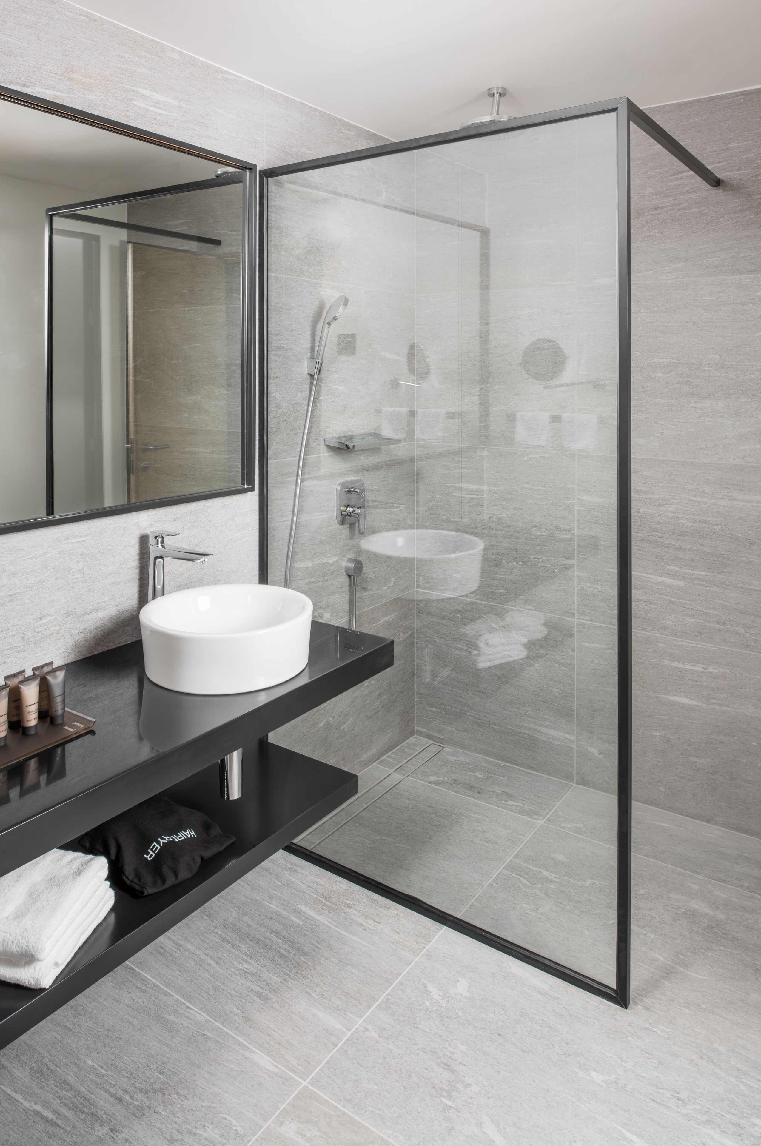 A modern bathroom with a glass-enclosed shower, a white sink, and a black countertop.