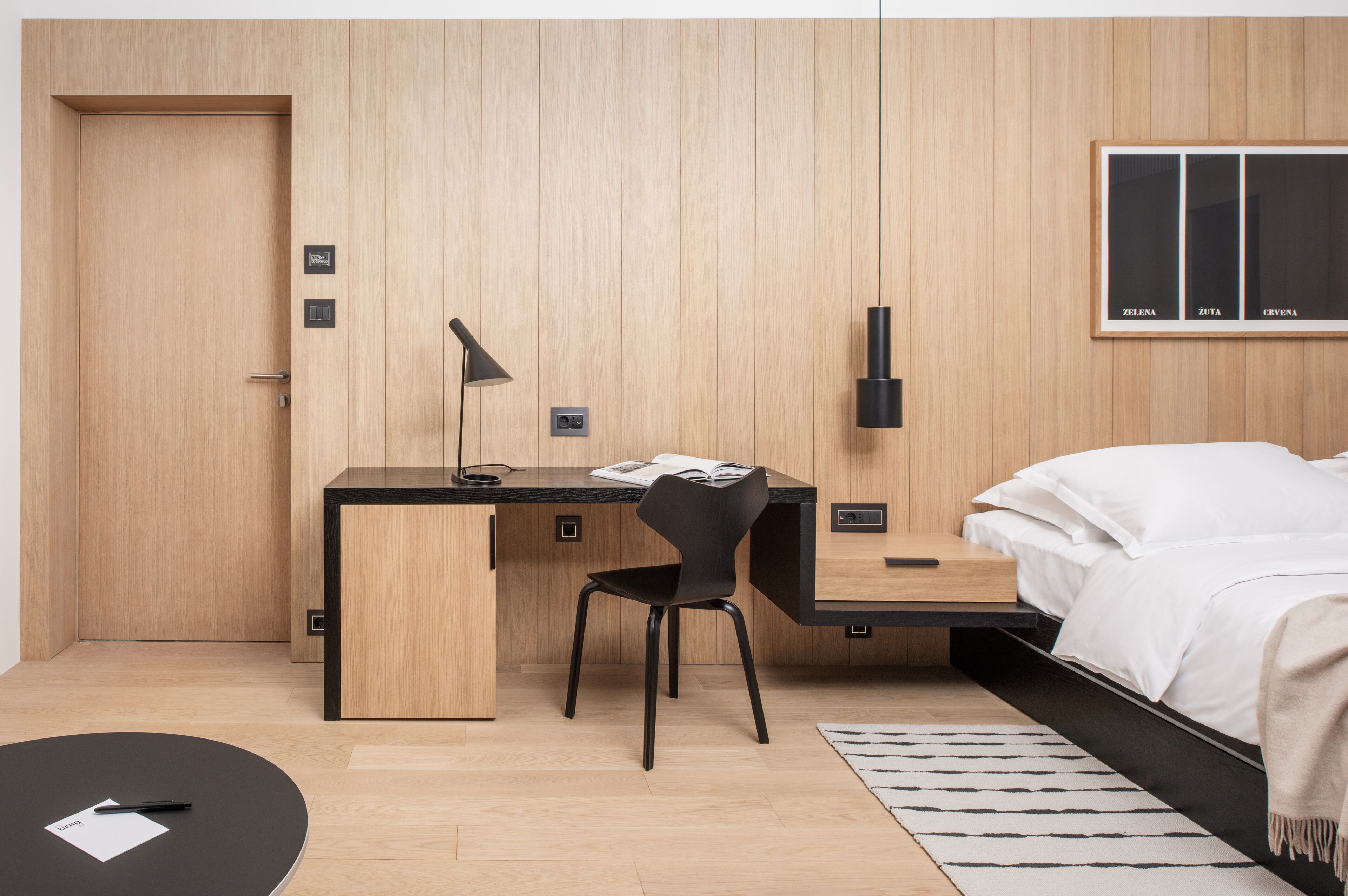 A modern bedroom with a wooden wall panel, a desk with a chair, a bed, and a bedside table.