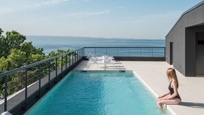 A poolside area with a view of the sea, lounge chairs, and a person sitting by the pool. - Briig Boutique Hotel (Split)