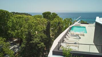 Una piscina en la azotea con sillones de descanso, rodeada de abundante vegetación y con vistas al mar.