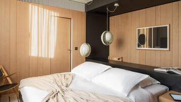 A modern bedroom with a large bed, wooden panel walls, a bedside table with a book, and a hanging light fixture.