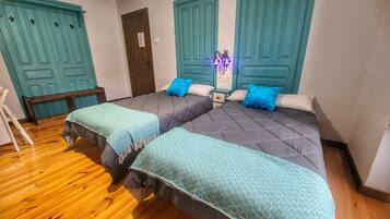 A room with two beds, teal-colored doors, a wooden bench, and a small table.