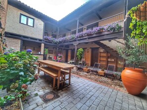 Une cour avec une table en bois et des bancs, entourée de plantes et de fleurs en pot.
