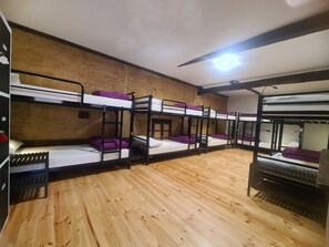 Une chambre de dortoir avec des lits superposés, un plancher en bois et un ventilateur de plafond.