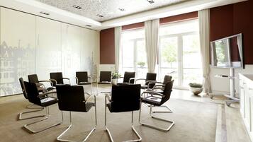 Un salón de conferencias de diseño moderno, con una mesa central rodeada de sillas negras con patas cromadas, ventanas amplias con cortinas y un televisor de pantalla plana montado en la pared.