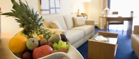 A fruit bowl on a table in a hotel room with a sofa, coffee table, and lamp in the background.