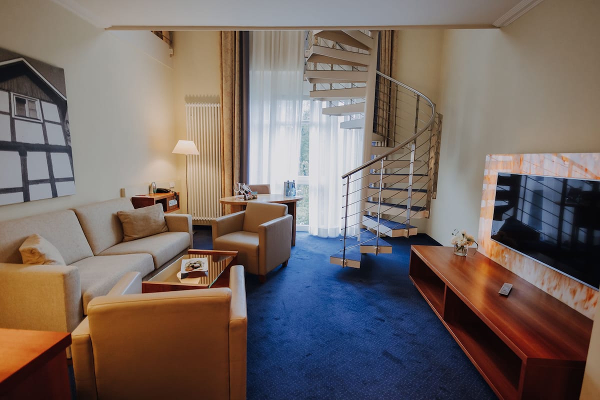 A modern living room with a sofa, armchairs, a coffee table, a TV, and a spiral staircase.