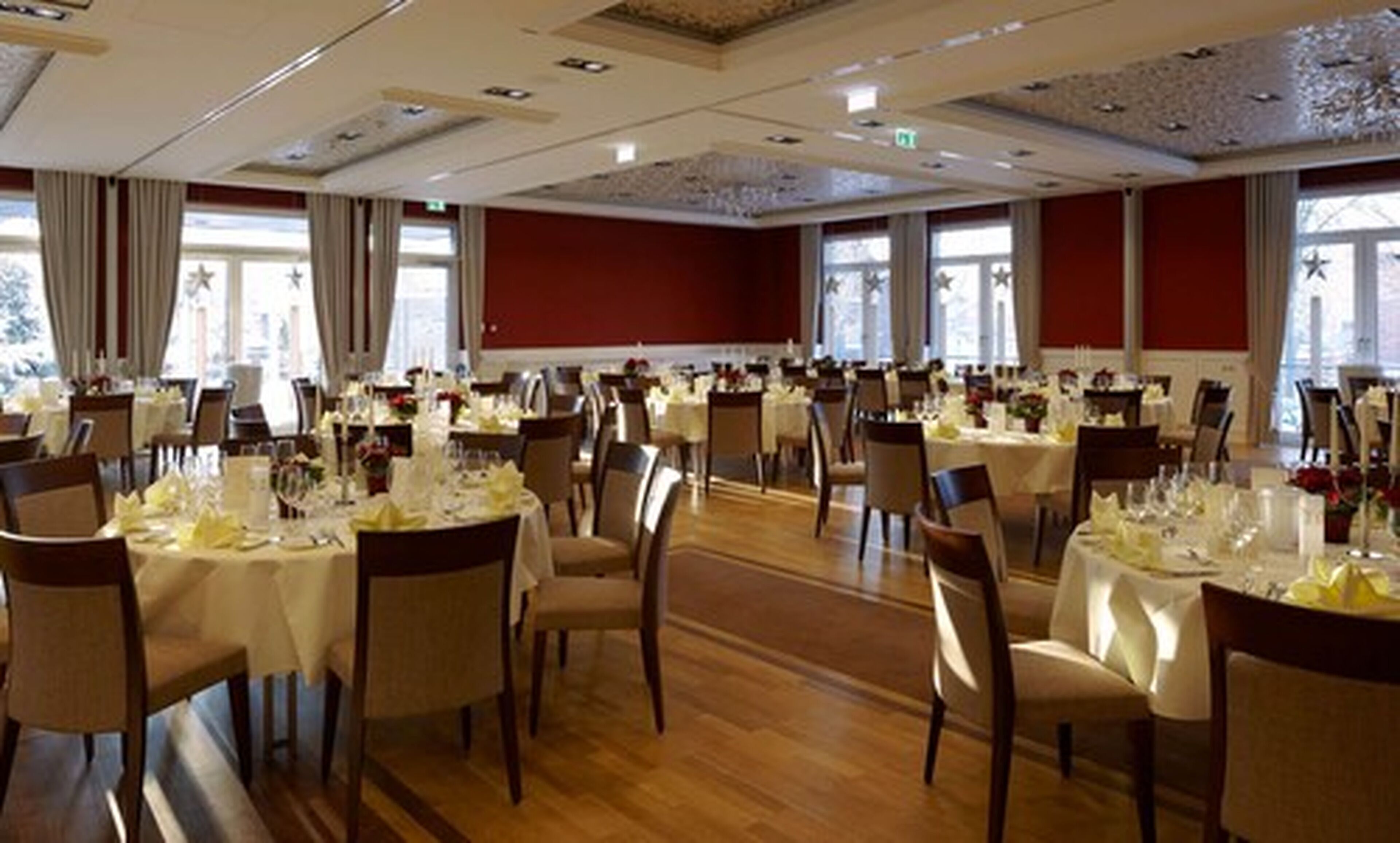 Un amplio salón de banquetes con varias mesas redondas dispuestas para comidas, con manteles blancos y sillas.