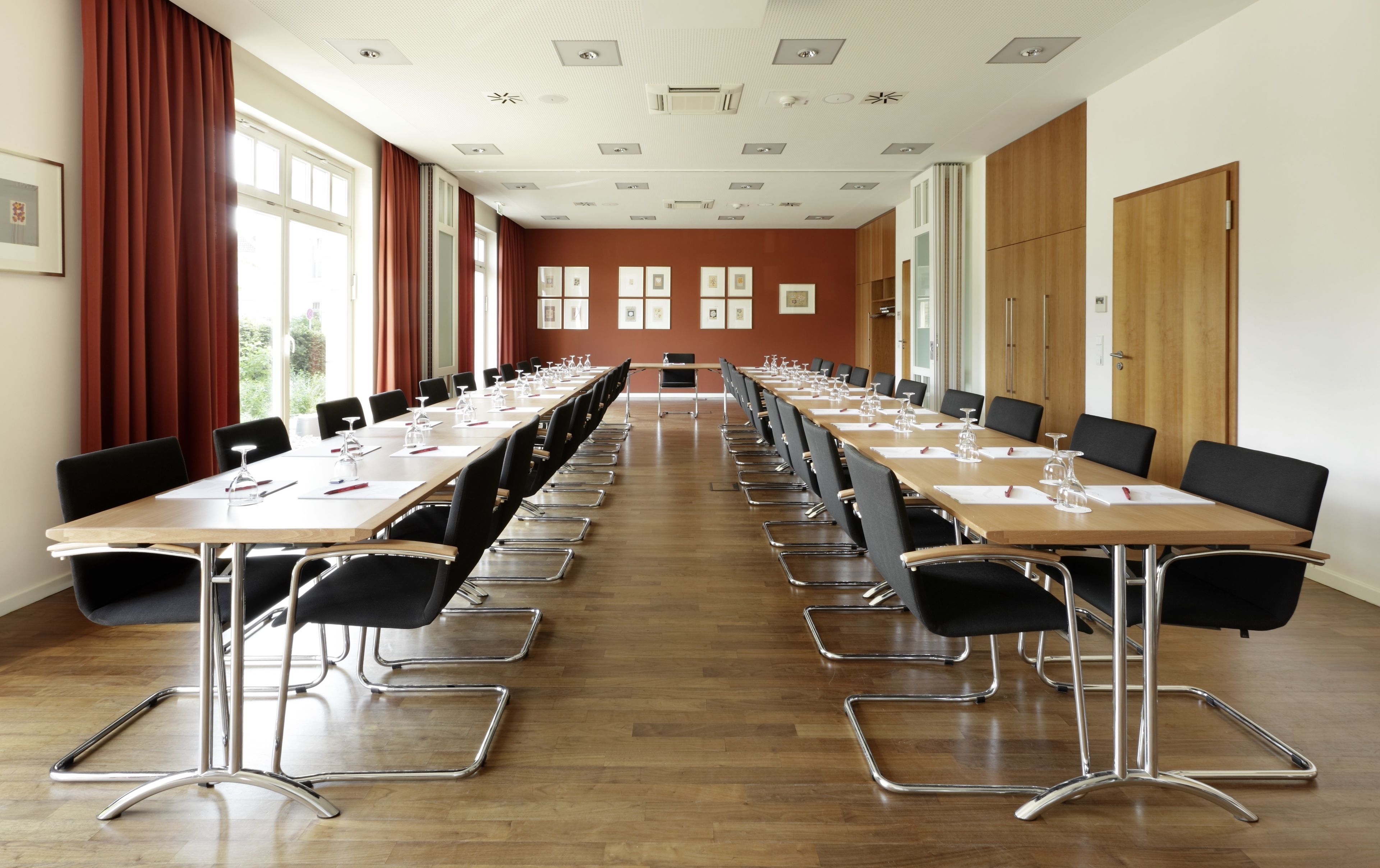 A conference room with long tables and chairs, large windows, and a wooden floor.