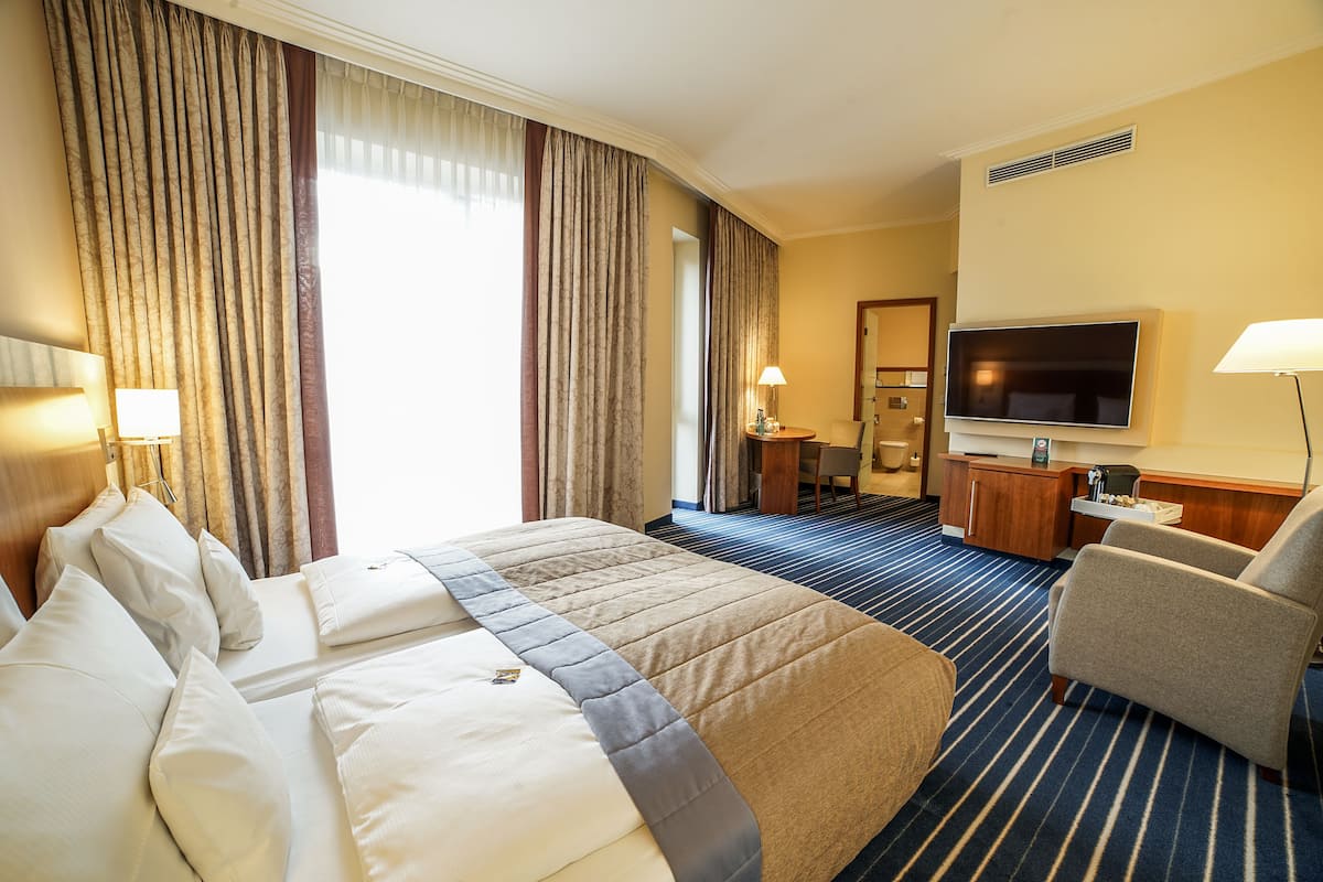 A hotel room with a large bed, a desk with a TV, a chair, and a bathroom visible through a door.