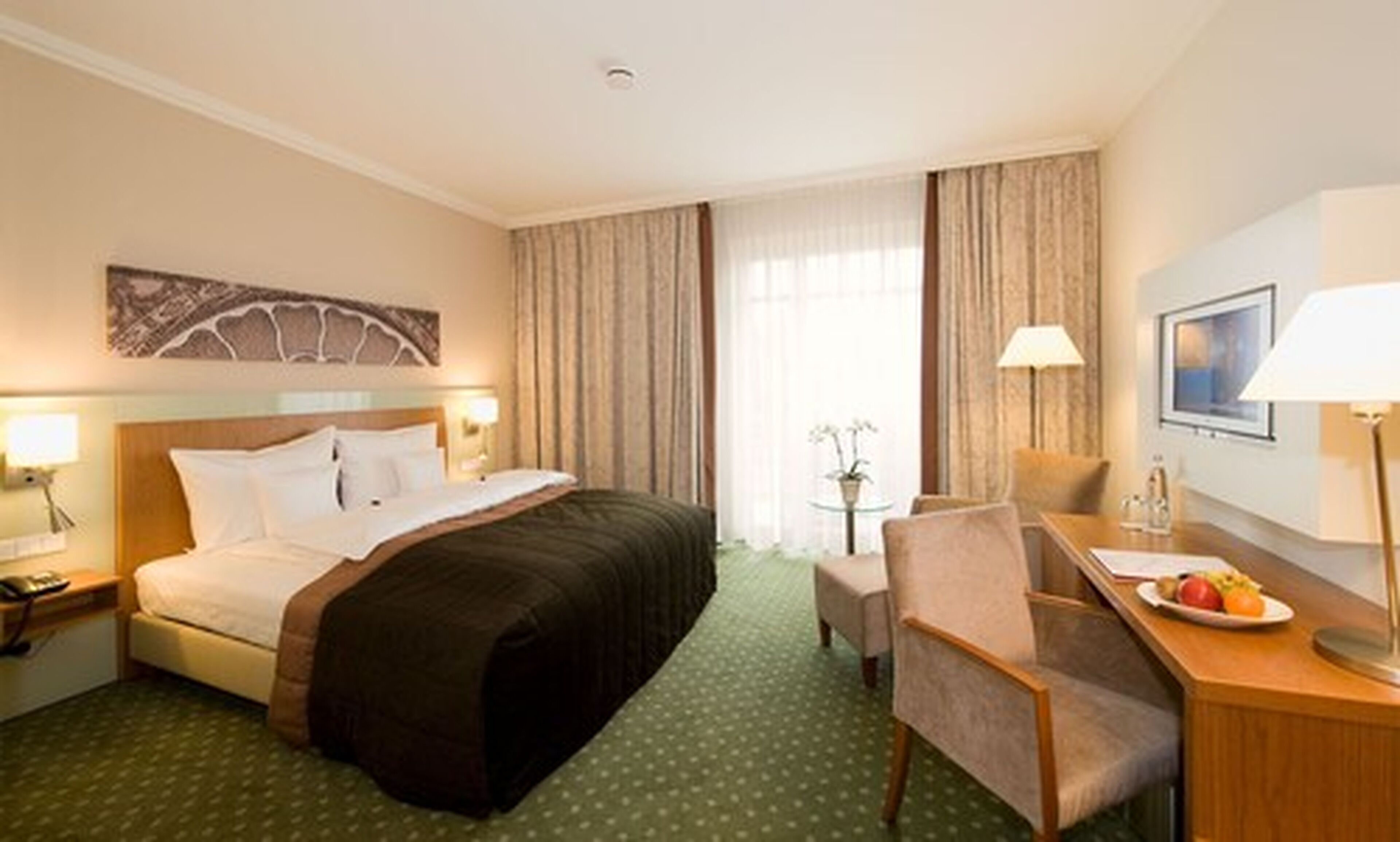 Ein Hotelzimmer mit einem Bett, einem Schreibtisch mit Stuhl, einer Lampe und einem kleinen Tisch mit Obst.