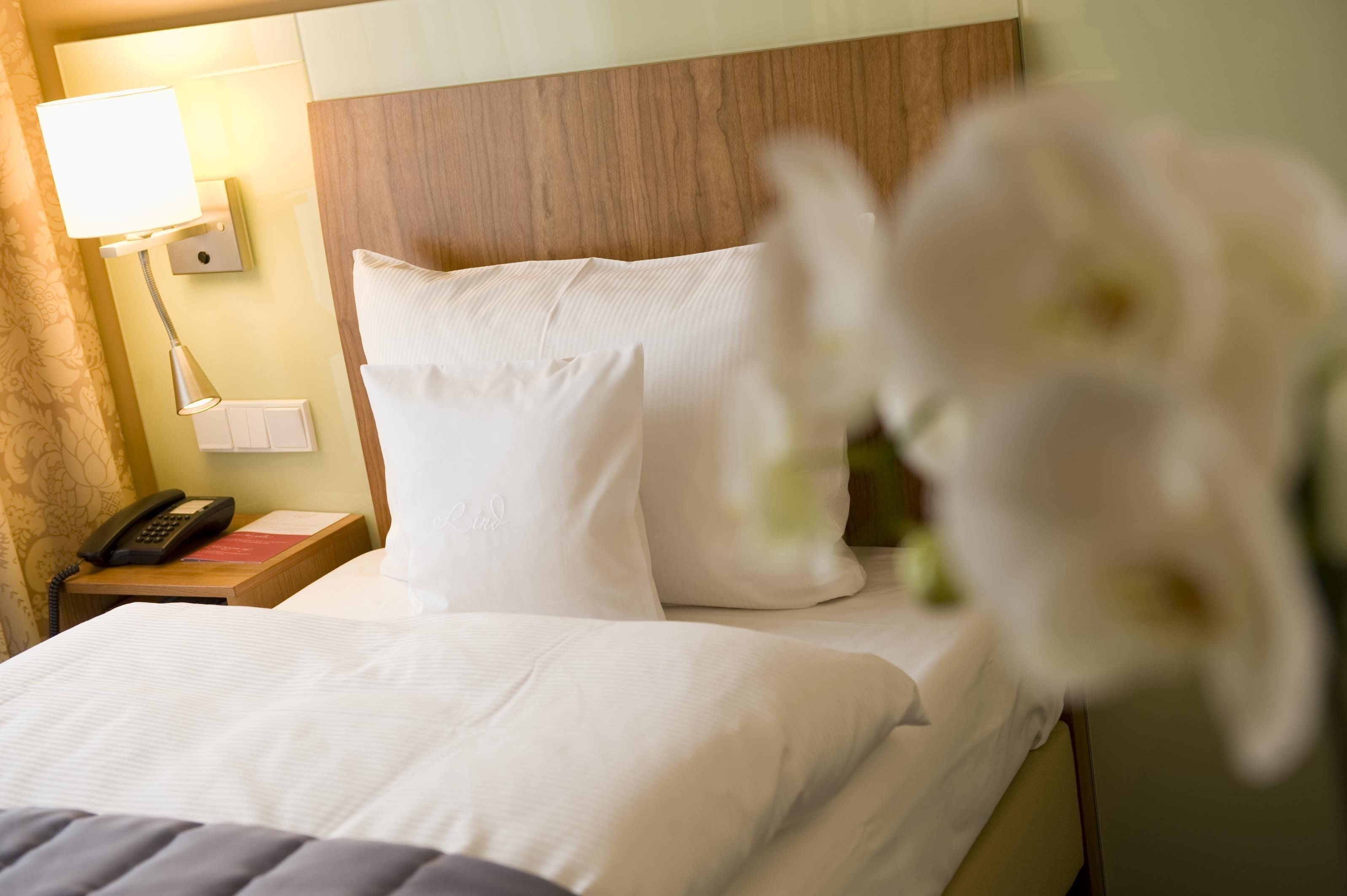 A hotel room with a neatly made bed, a bedside lamp, a phone, and a nightstand.