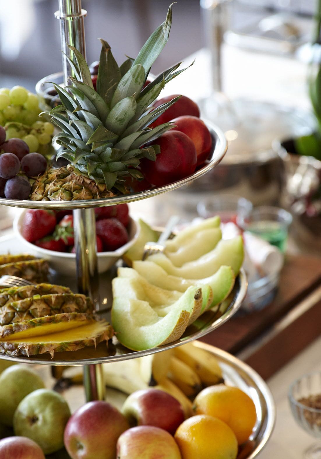 A multi-tiered fruit stand with various fruits like grapes, pineapple, apples, and bananas.