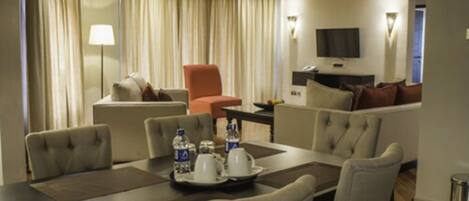 A hotel room with a dining area, a sofa, a TV, and a lamp.