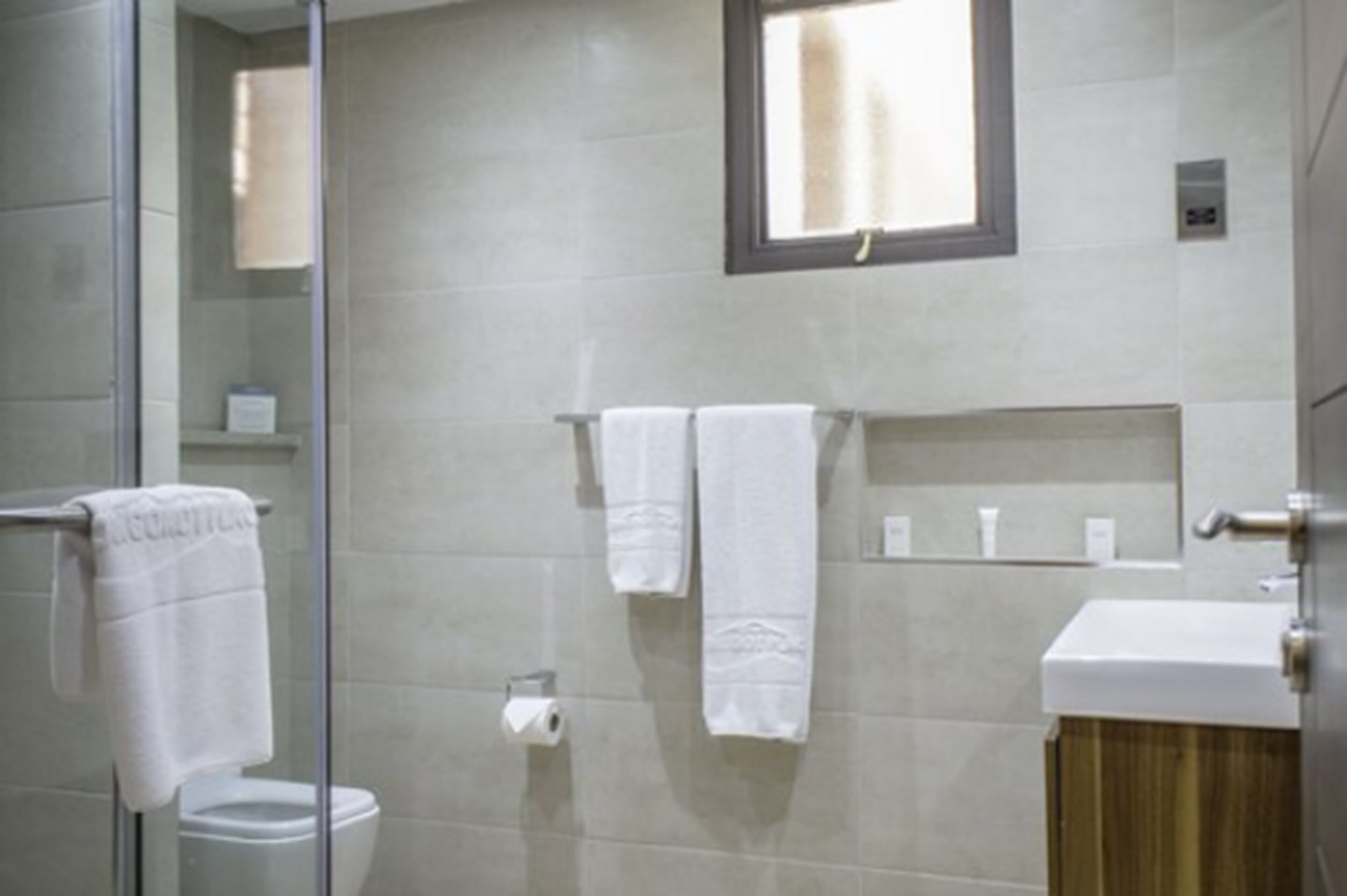 A bathroom with a glass shower enclosure, a toilet, a sink with a wooden cabinet, and a towel rack with two towels.
