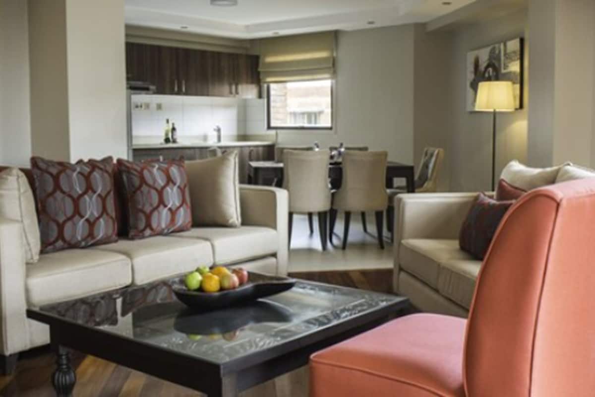 A modern living room with a sofa, armchair, and coffee table. There is a dining area with chairs and a table in the background.