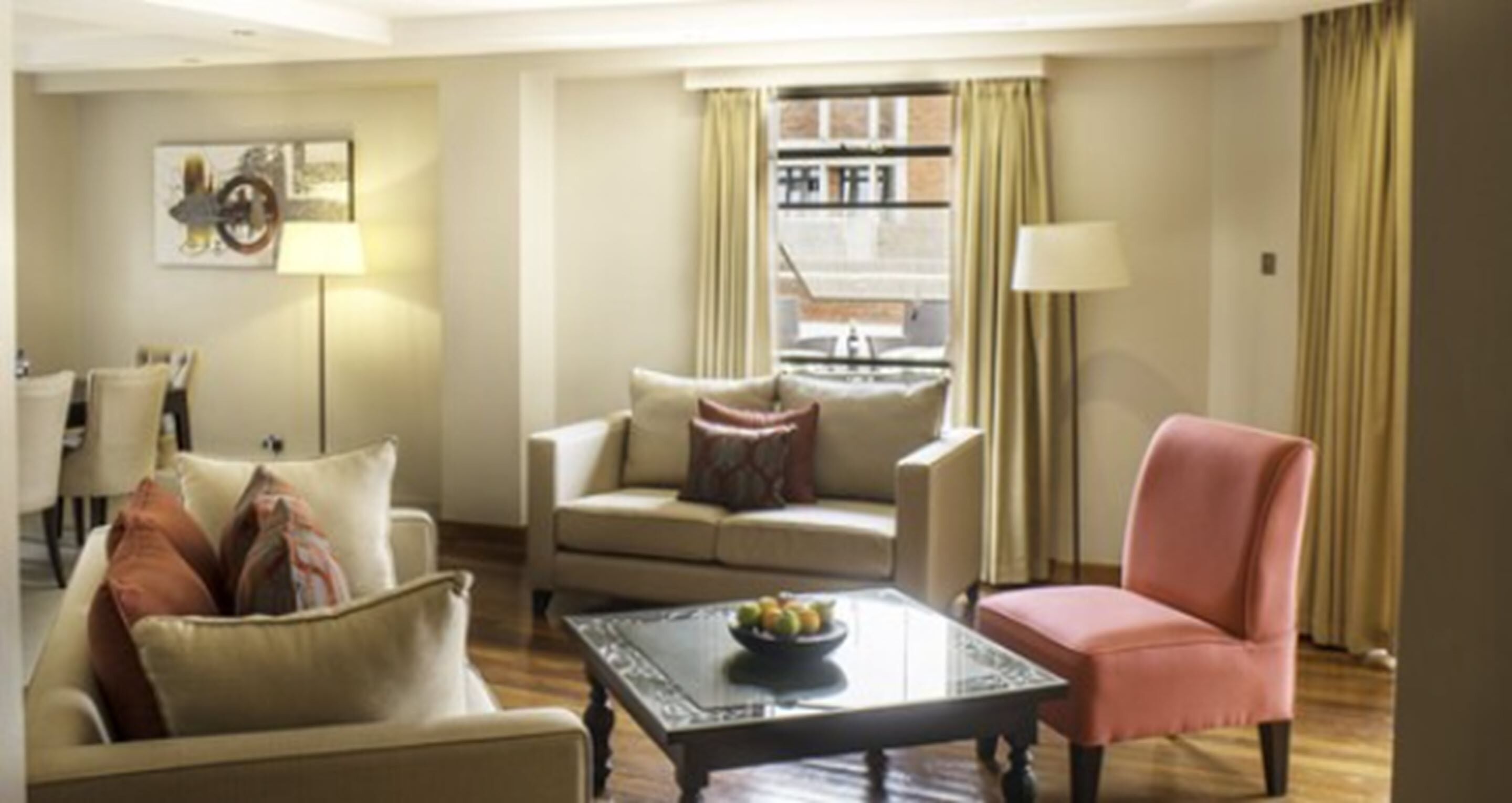 A living room with a sofa, armchair, and coffee table. There is a window with curtains and a lamp on a side table.