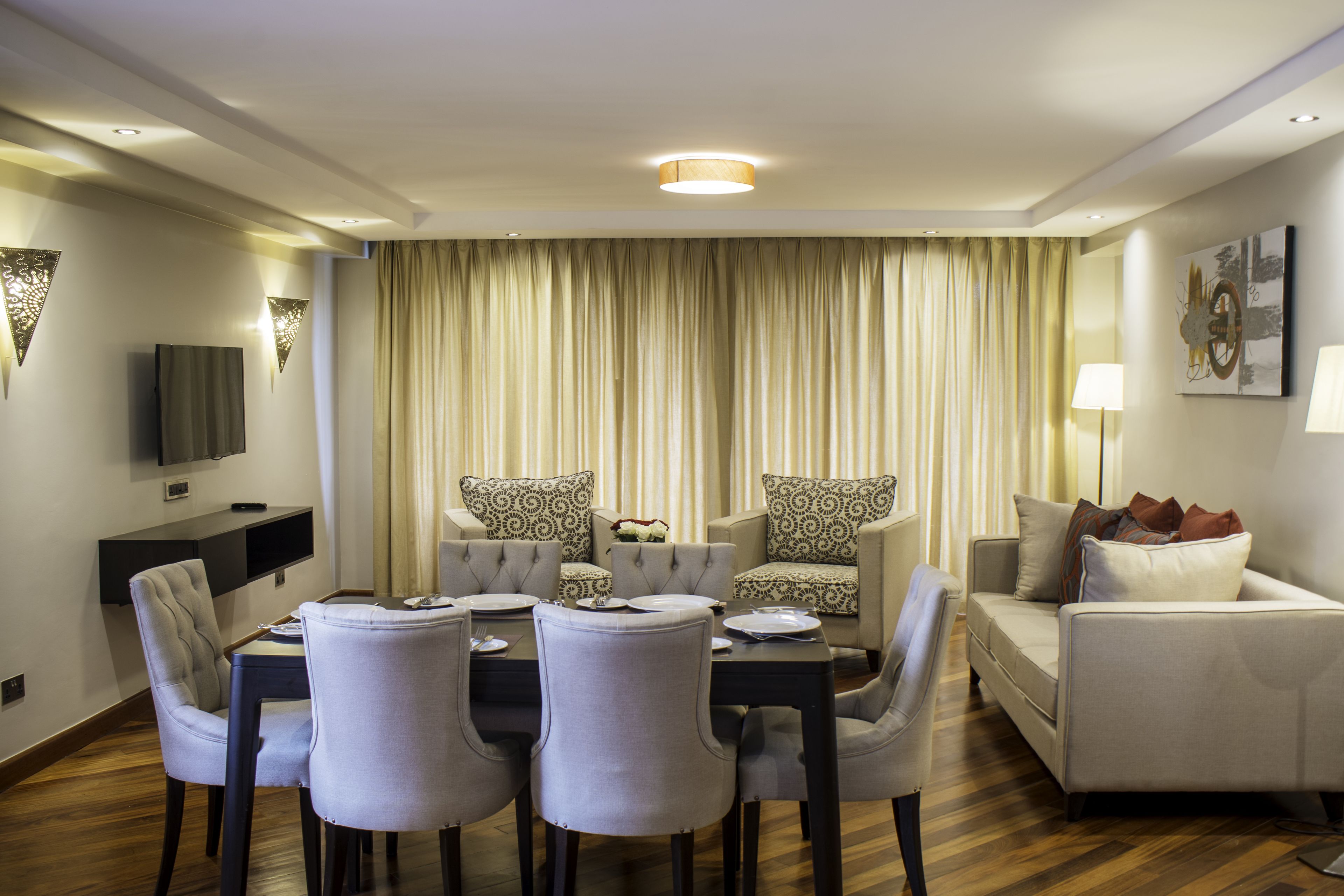 Una sala de estar moderna con comedor, que incluye un sofá, dos sillones, una mesa de centro y un televisor de pantalla plana montado en la pared.