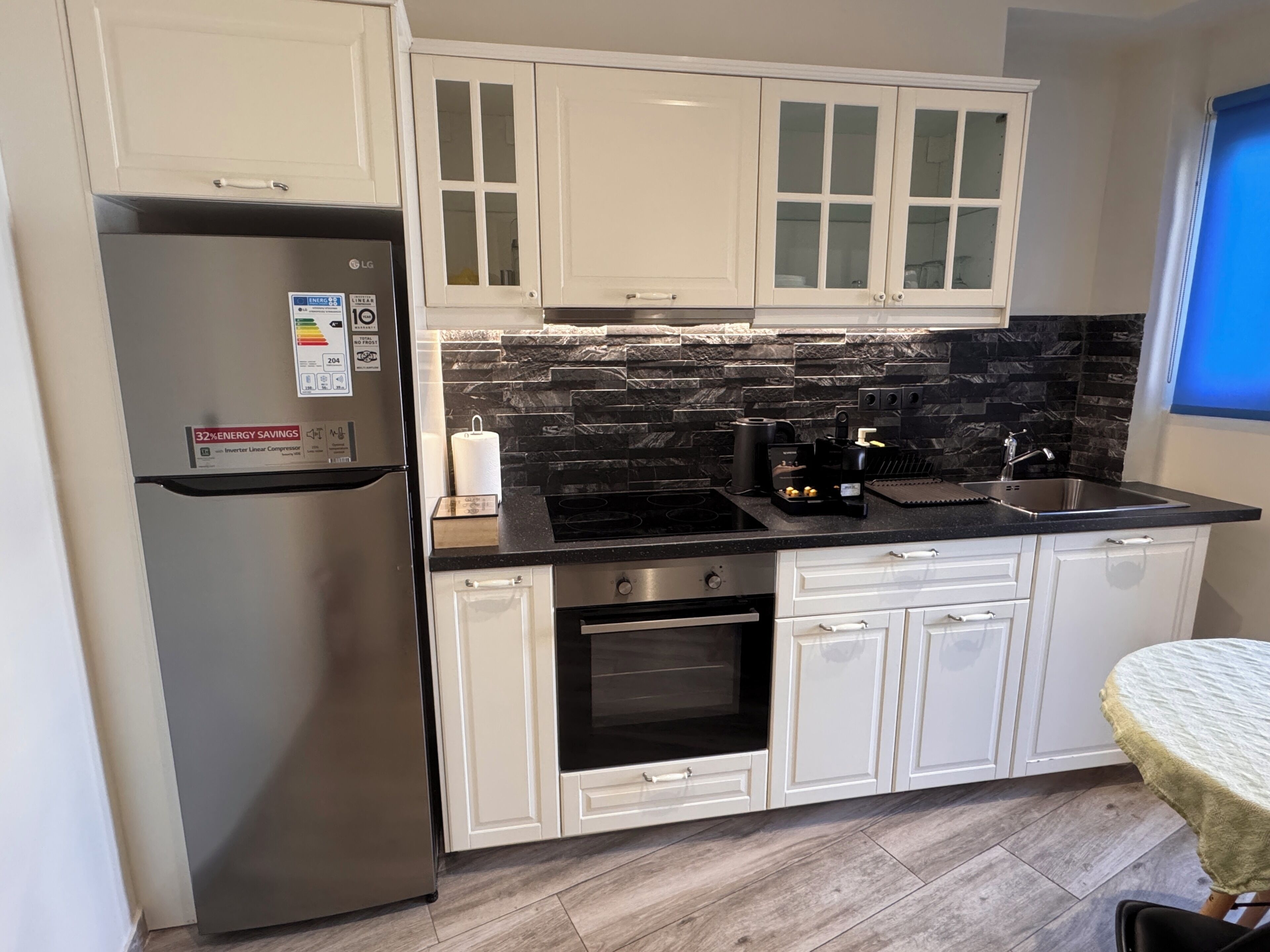 A modern kitchen with white cabinets, a stainless steel refrigerator, a black countertop, and a stone backsplash.