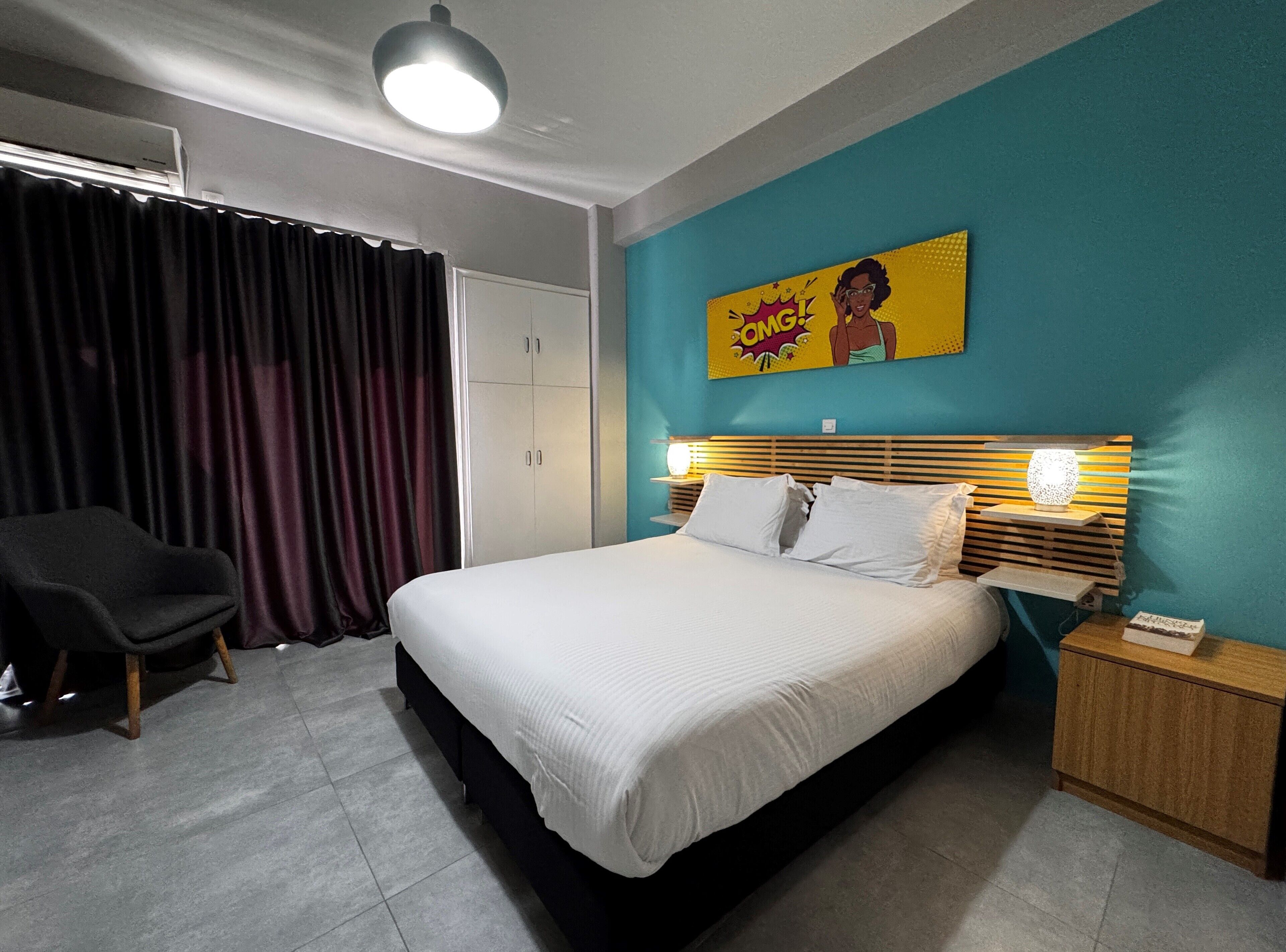 Un dormitorio con una cama, una silla, una mesita de noche y un cuadro de arte pop en la pared.