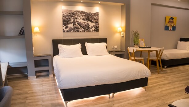 A modern hotel room with a large bed, bedside tables, a small dining table, and a chair. - Connect Studios & Apartments (Athens)