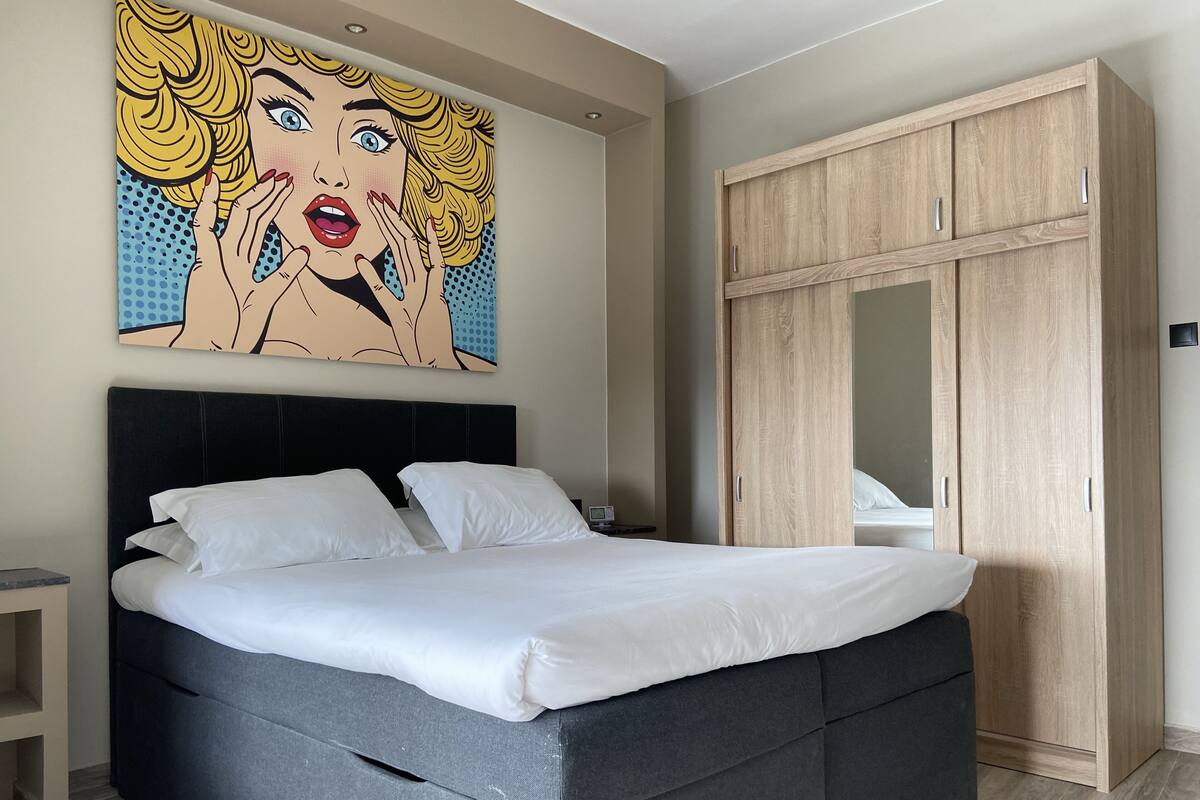 Un dormitorio con cama, armario y un cuadro de arte pop en la pared.